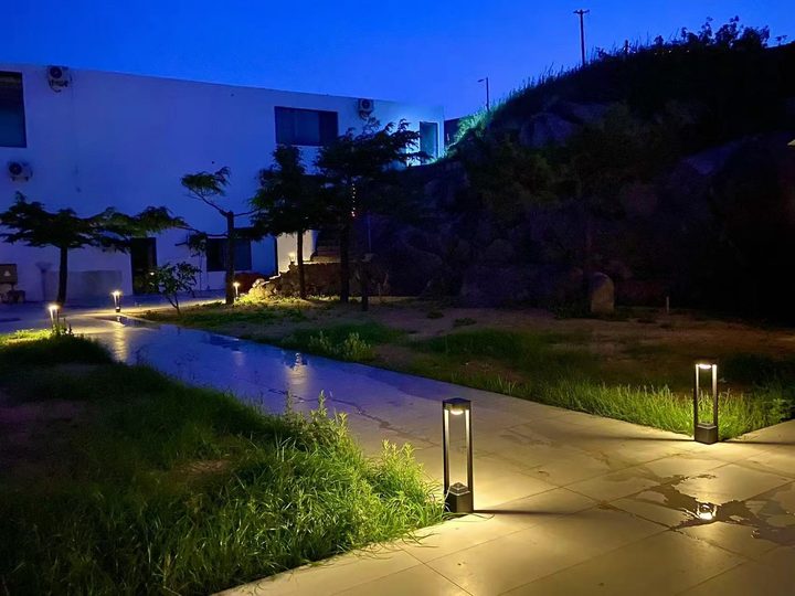 Illuminated rectangular open-frame bollards along wet garden paths