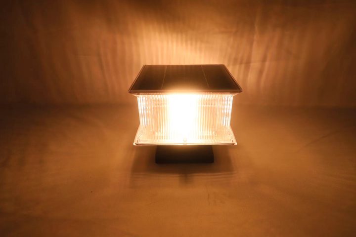 Square ribbed lamp pictured illuminated with a warm appearance in a studio.