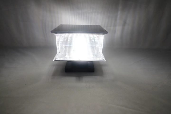 Square ribbed lamp pictured illuminated with a white appearance in a studio.
