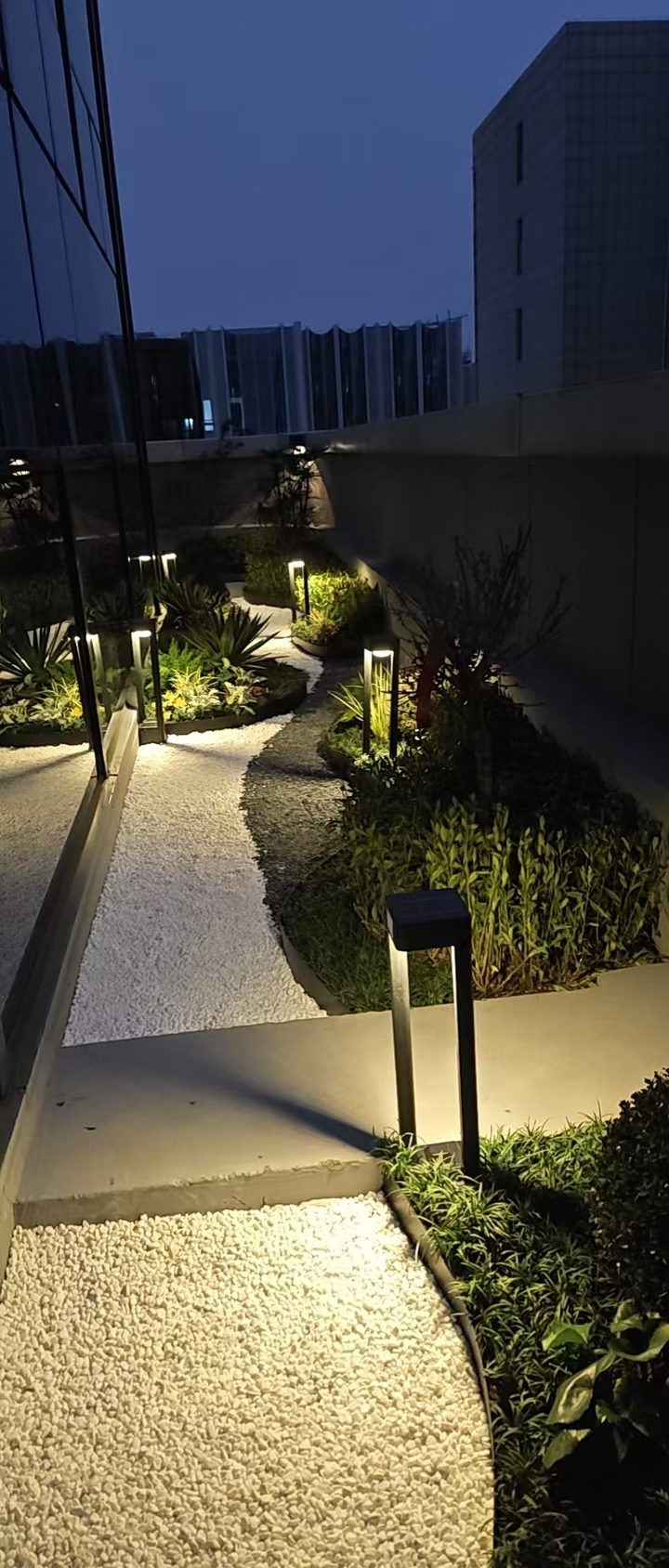 Factory-supplied reference showing open-frame bollards along a planted courtyard path.